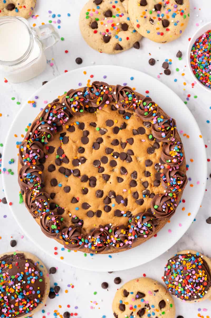 chocolate chip cookie cake with frosting and sprinkles on a white serving plate