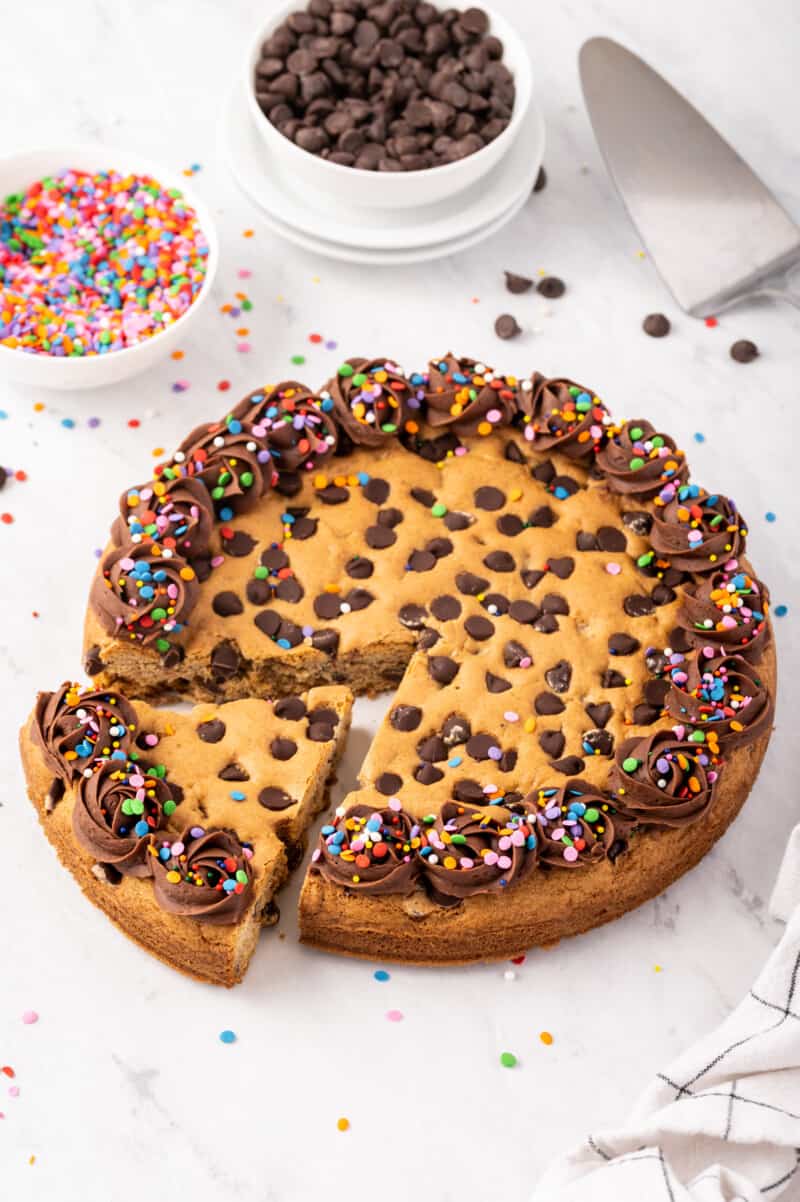 chocolate chip cookie cake with chocolate frosting and sprinkles with a slice cut out