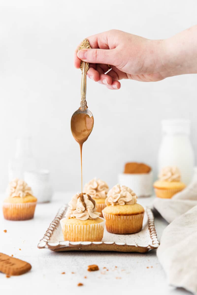 hand using a spoon to drizzle cookie butter onto cookie butter cupcakes