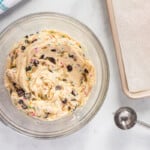 cake batter cookie dough in a bowl with a cookie scoop and a parchment paper lined baking sheet