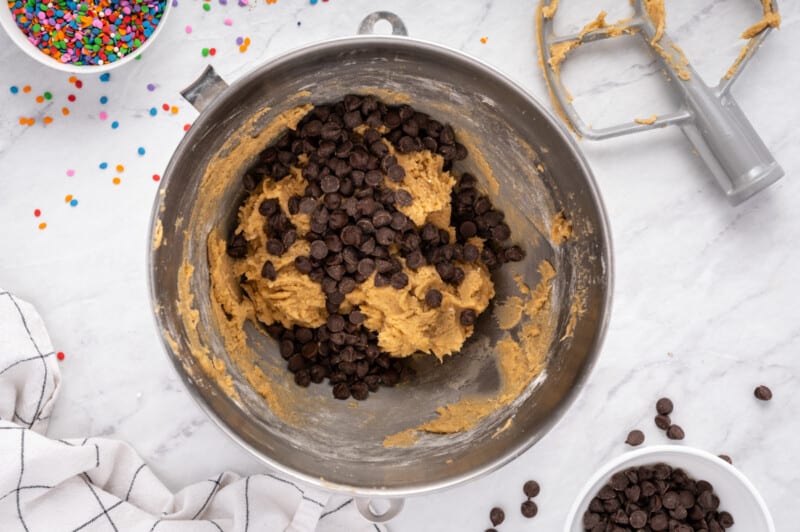 chocolate chips added to cookie cake batter in a metal bowl