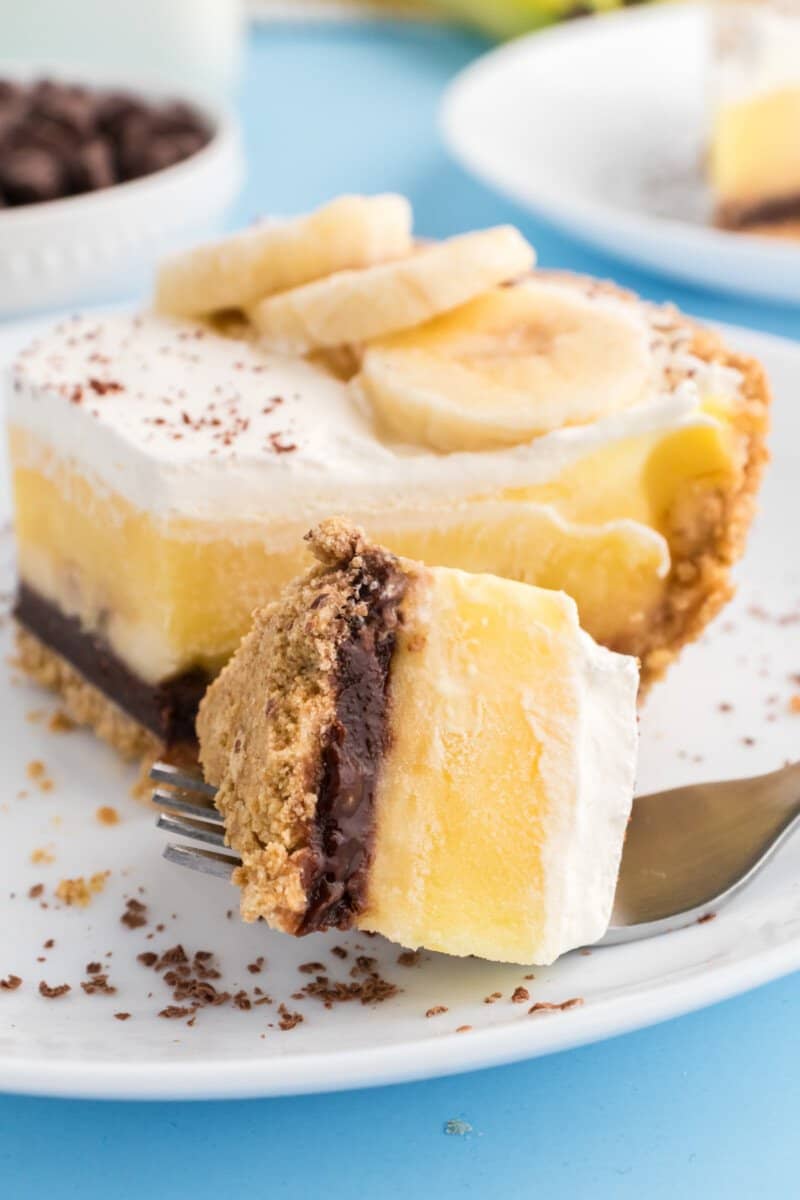 a forkful of banana fudge pie resting next to a slice on a white plate.
