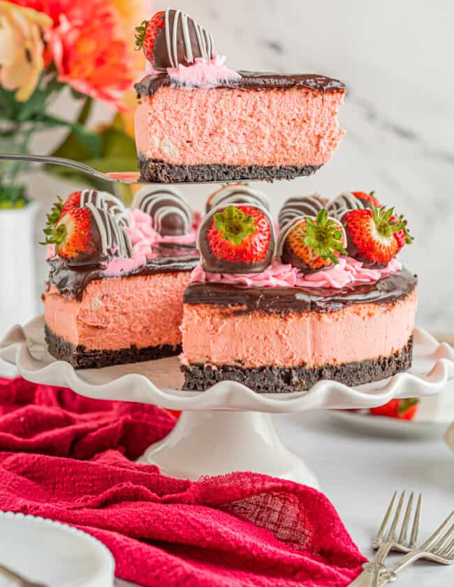 a slice of chocolate covered strawberry cheesecake on a cake server above a chocolate covered strawberry cheesecake.