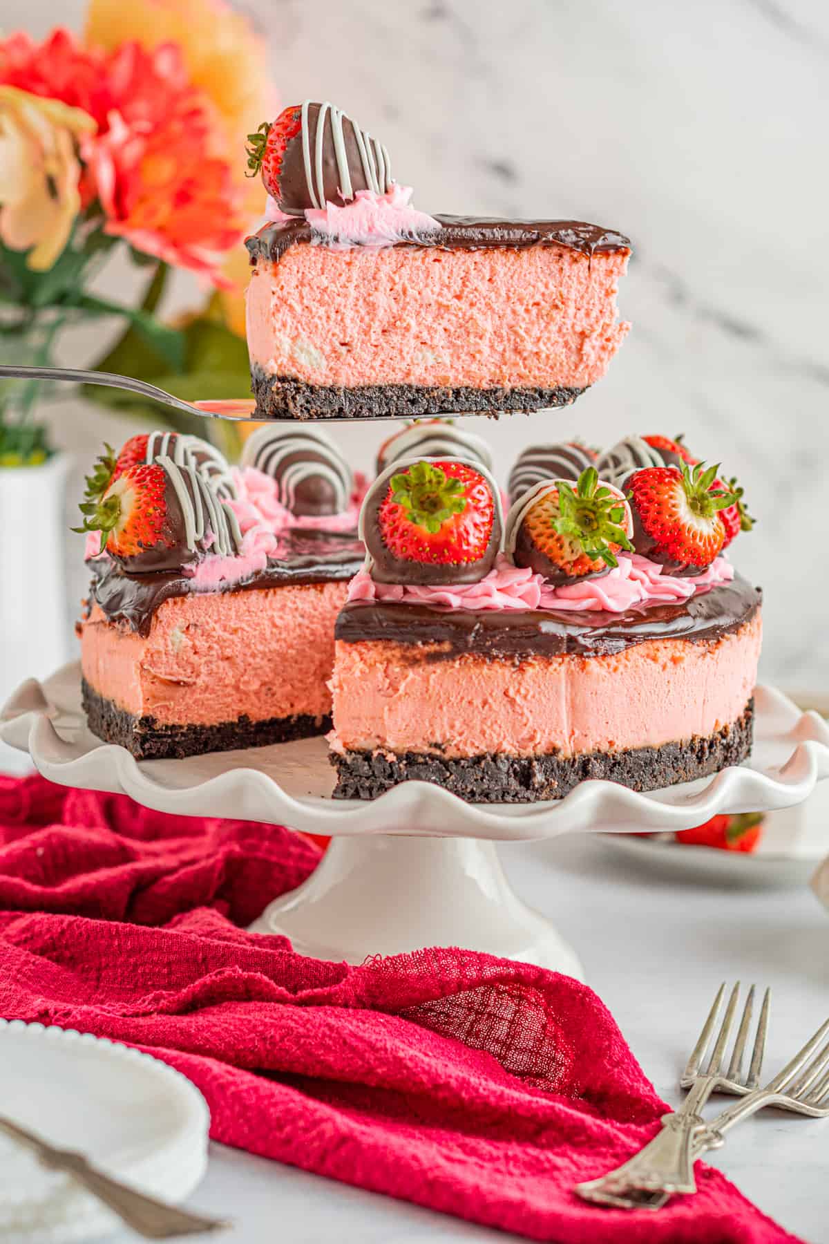 a slice of chocolate covered strawberry cheesecake on a cake server above a chocolate covered strawberry cheesecake.