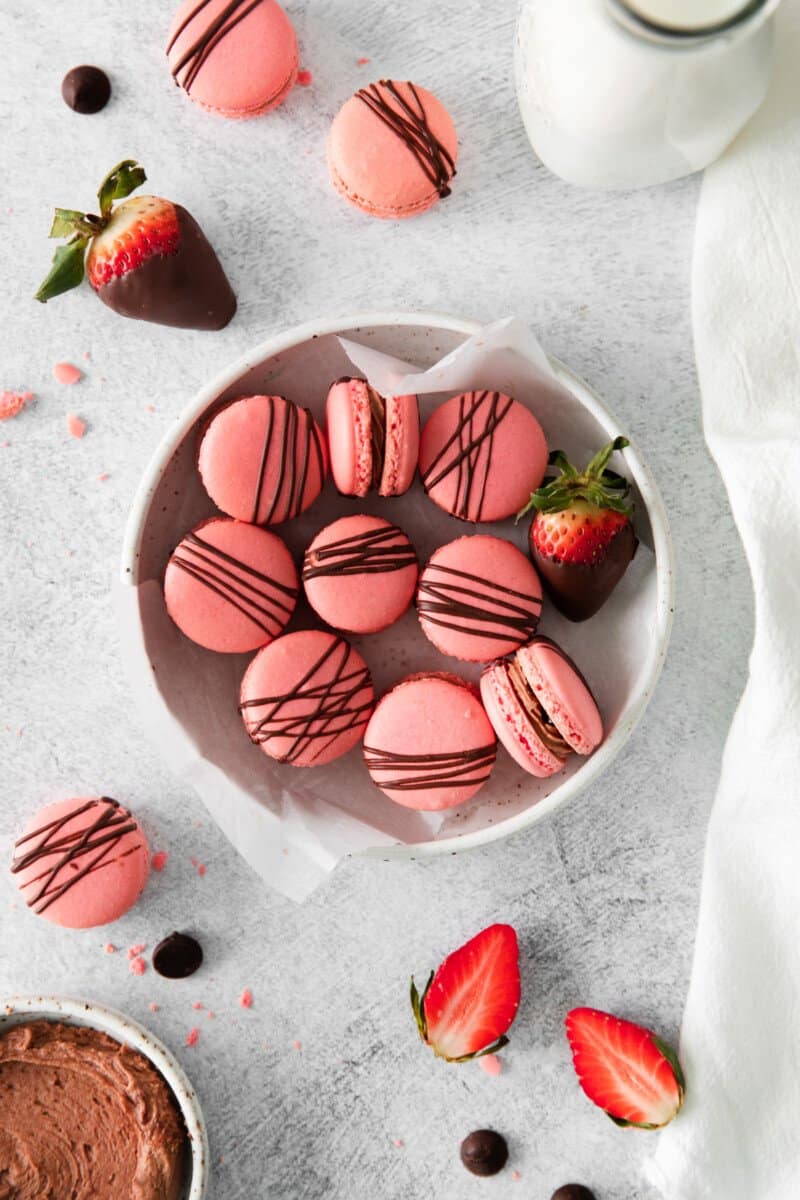overhead view of chocolate strawberry macarons in a white bowl.