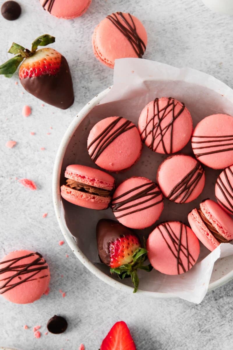 close up of chocolate strawberry macarons in a white bowl.