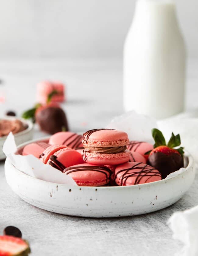 chocolate strawberry macarons in a white bowl with a jug of milk.