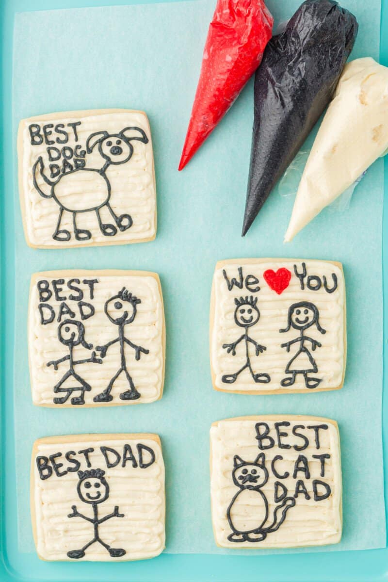 5 fathers day cookies on a blue baking sheet with red black and white frosting.