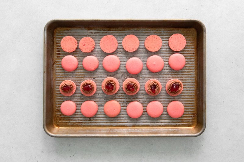 overhead view of chocolate buttercream piped onto macaron shells and filled with jam on a baking sheet.