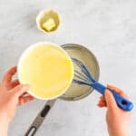 pastry cream mix poured into a saucepan with a blue whisk.