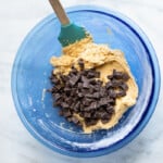 chocolate chunks added to cookie dough in a blue bowl with a spatula