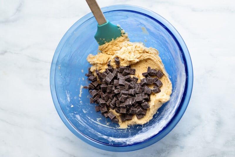 chocolate chunks added to cookie dough in a blue bowl with a spatula