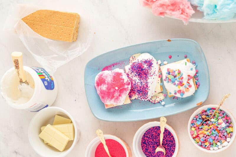 sprinkles on top of cotton candy on top of white chocolate bars and graham crackers on a blue plate