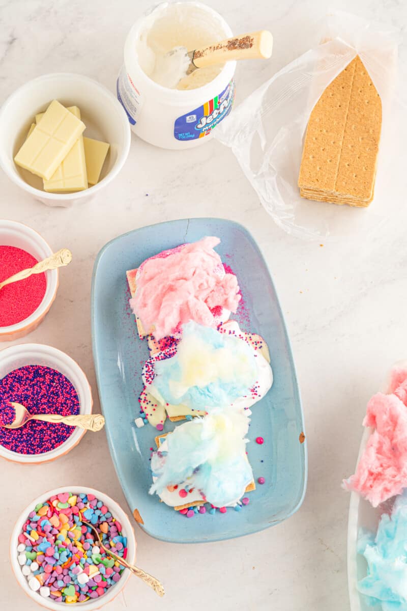 cotton candy and sprinkles on top of white chocolate and graham crackers on a blue plate