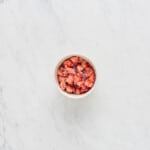 overhead view of strawberries and sugar macerating in a white bowl.