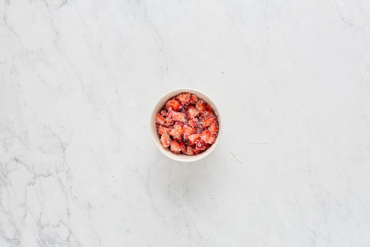 overhead view of strawberries and sugar macerating in a white bowl.