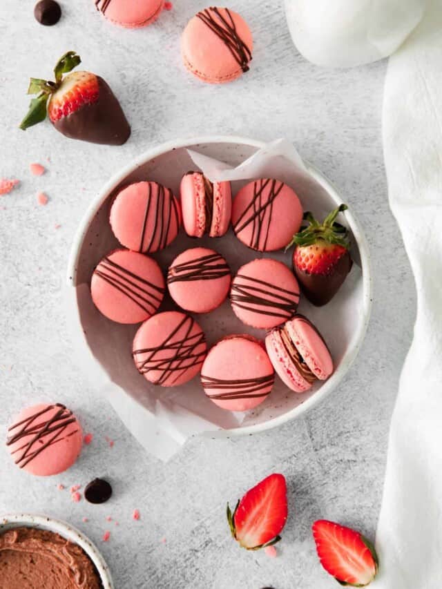 overhead view of chocolate strawberry macarons in a white bowl.