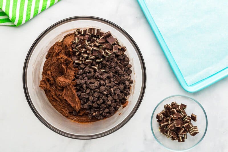 dry ingredients and chocolate chips added to andes mint cookie dough in a glass bowl.