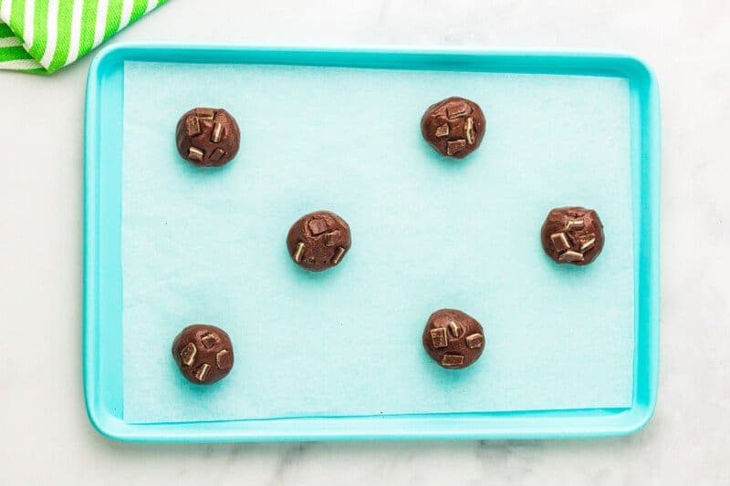 6 andes mint cookie dough balls on a blue baking sheet.