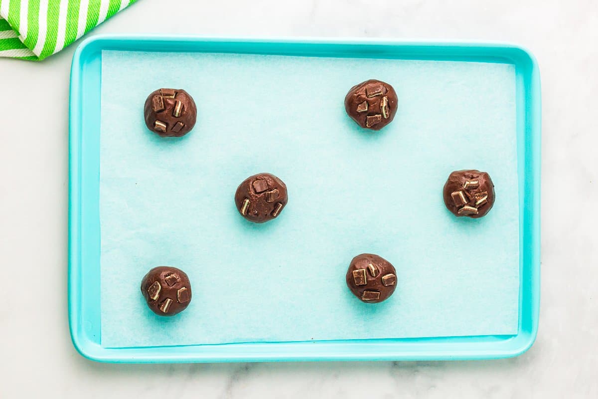 6 andes mint cookie dough balls on a blue baking sheet.