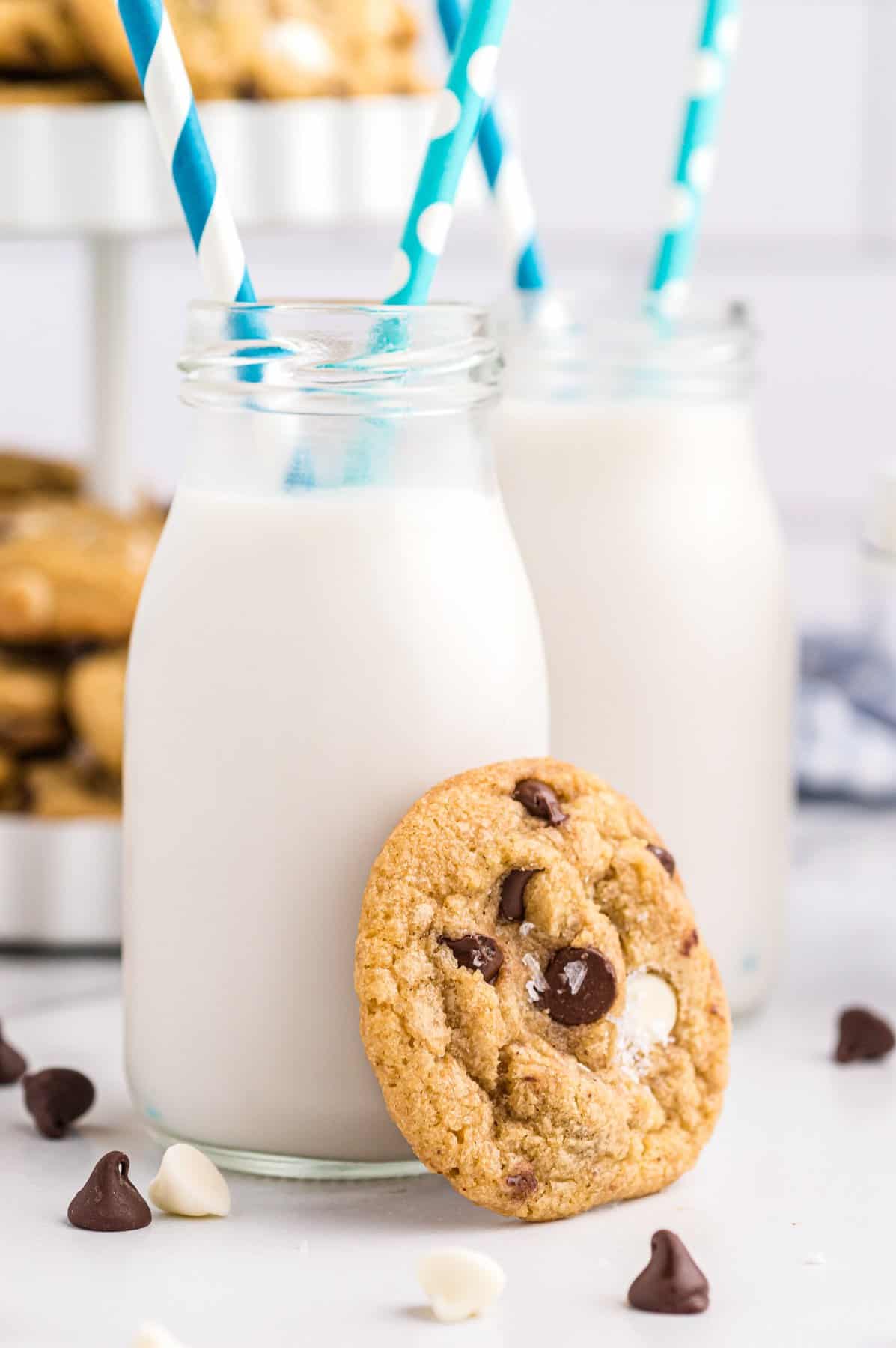 brown butter chocolate chip cookie leaning against a glass of milk with a blue and white straw.
