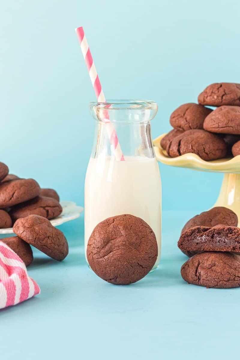 chocolate pudding cookie leaning against a glass of milk with a red and white straw.
