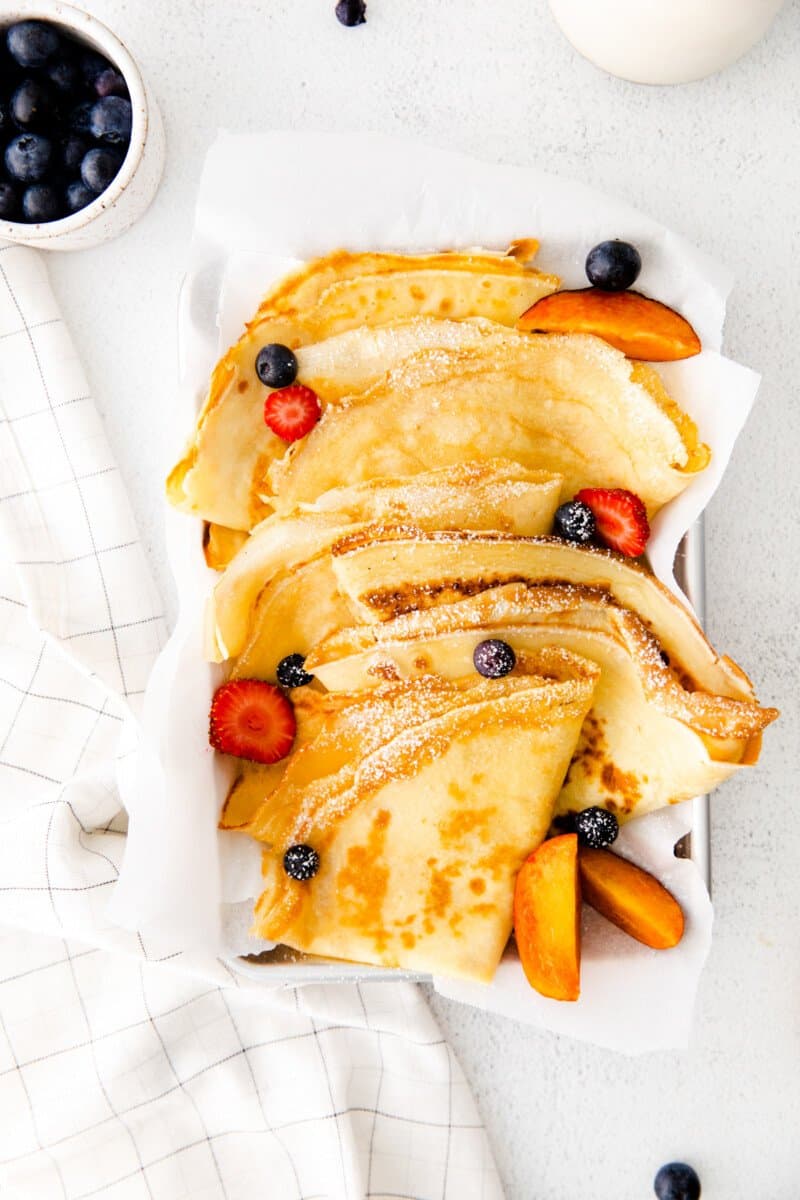 folded crepes on a white serving tray with fruit.