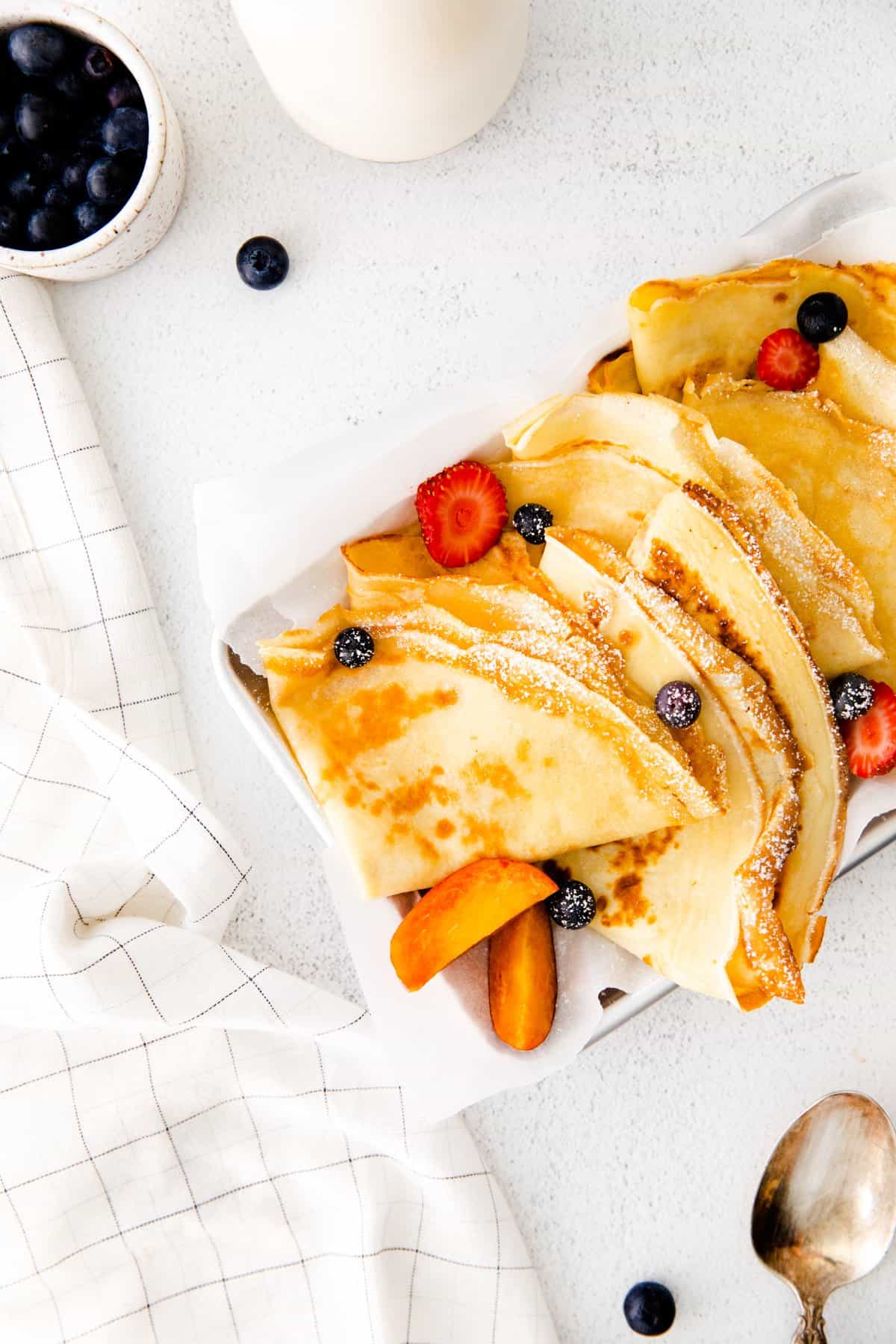 folded crepes on a white serving tray with fruit.