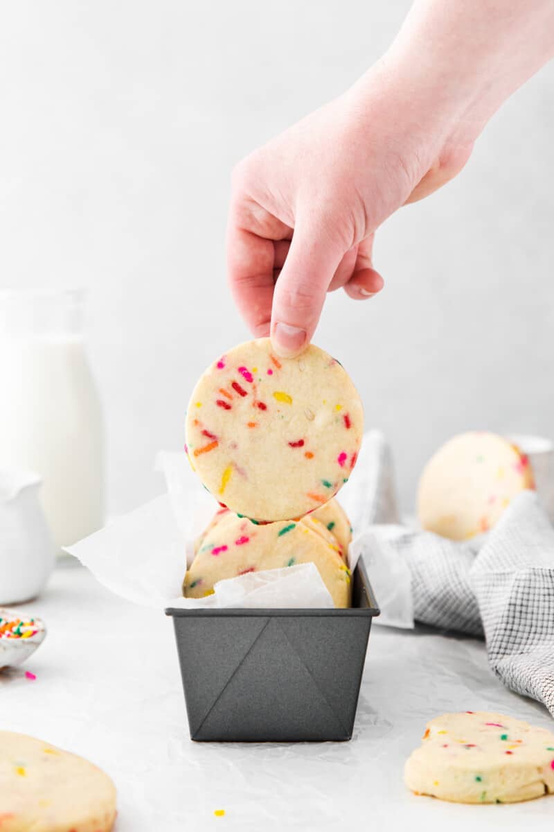 hand grabbing a funfetti shortbread cookie from a metal tin.