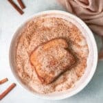 french toast slice dipped in cinnamon sugar mixture in a white bowl.