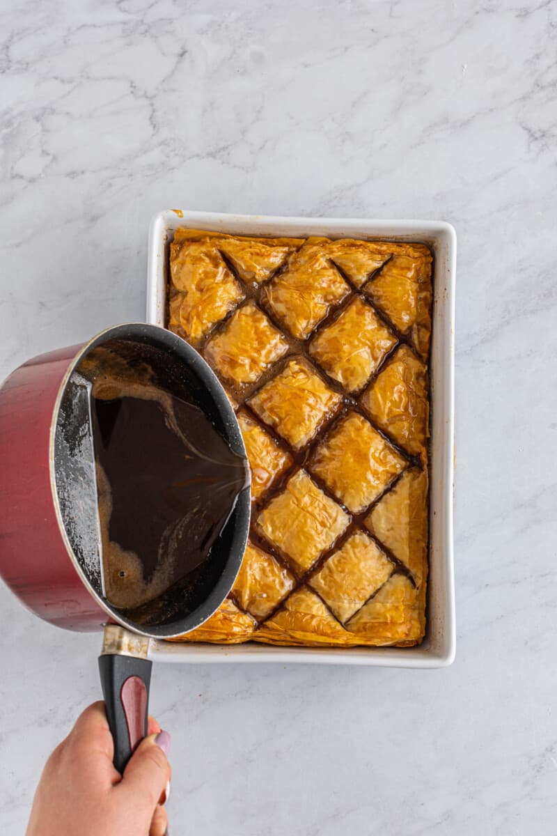syrup poured over baked homemade baklava in a baking pan.