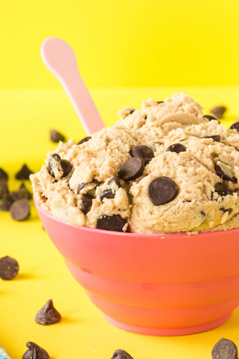 close up of edible chocolate chip cookie dough in a red bowl with a pink spoon.