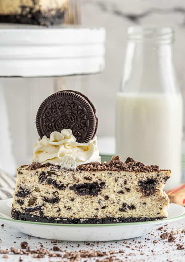 profile view of a slice of cookies and cream cheesecake on a white plate.
