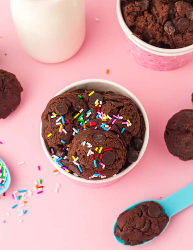 overhead view of edible brownie batter in a pink cup with a blue spoon and sprinkles.