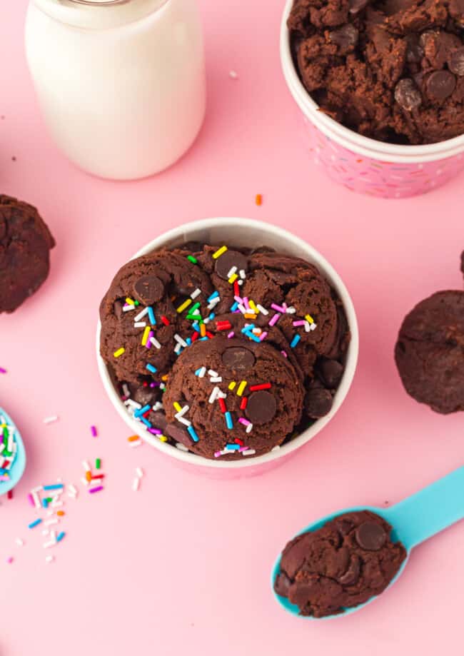 overhead view of edible brownie batter in a pink cup with a blue spoon and sprinkles.