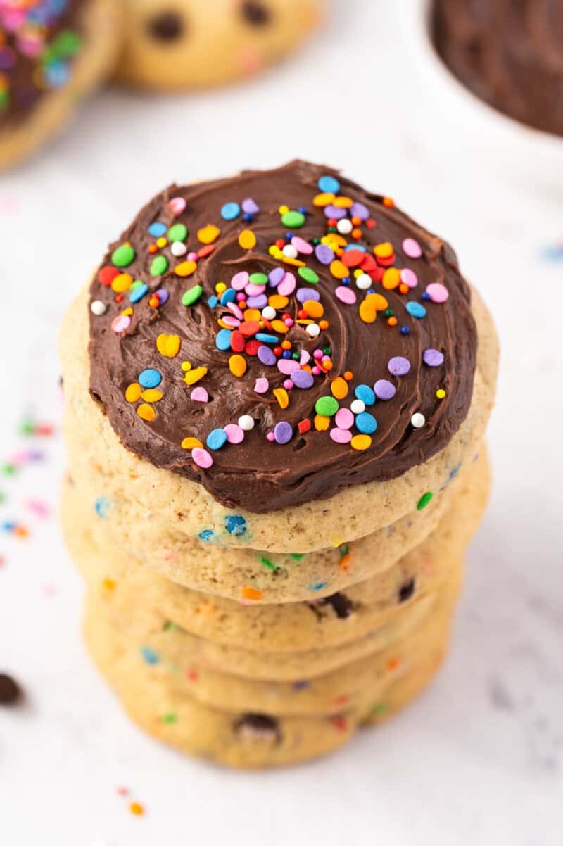 overhead view of a frosted chocolate chip cookie on top of a stack of 5 chocolate chip cookies.