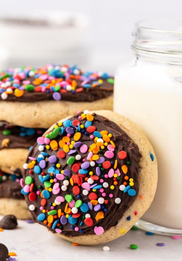 a frosted chocolate chip cookie leaning against a mason jar filled with milk.