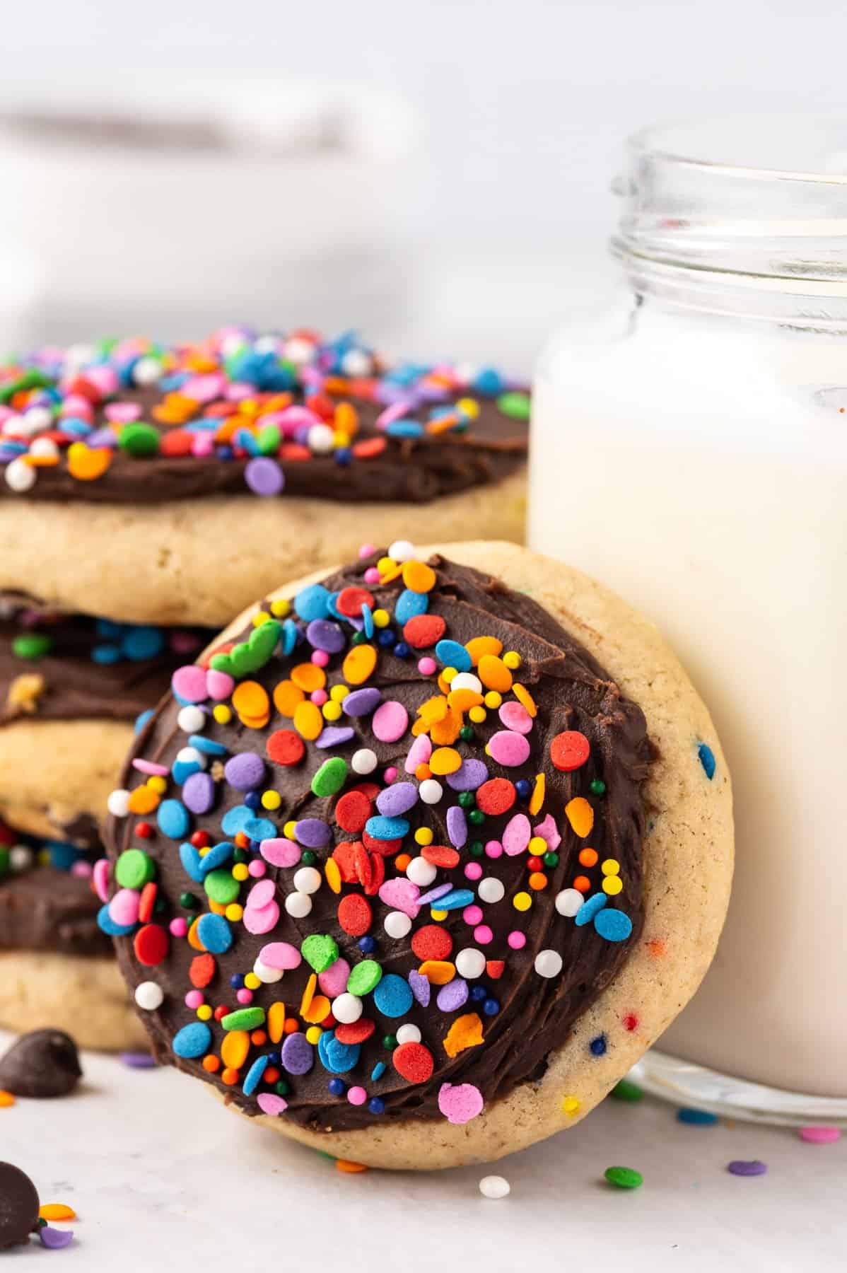 a frosted chocolate chip cookie leaning against a mason jar filled with milk.