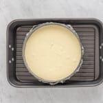 overhead view of creme brulee cheesecake batter in a springform pan wrapped in aluminum foil and set in a roasting pan.
