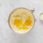 overhead view of eggs added to cheesecake batter in a stainless mixing bowl.