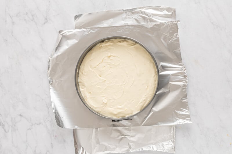 overhead view of double crust cheesecake batter in a springform pan on top of sheets of aluminum foil.