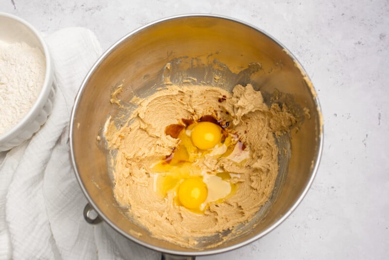overhead view of eggs and vanilla added to easter basket cookie cup dough in a stainless mixing bowl.