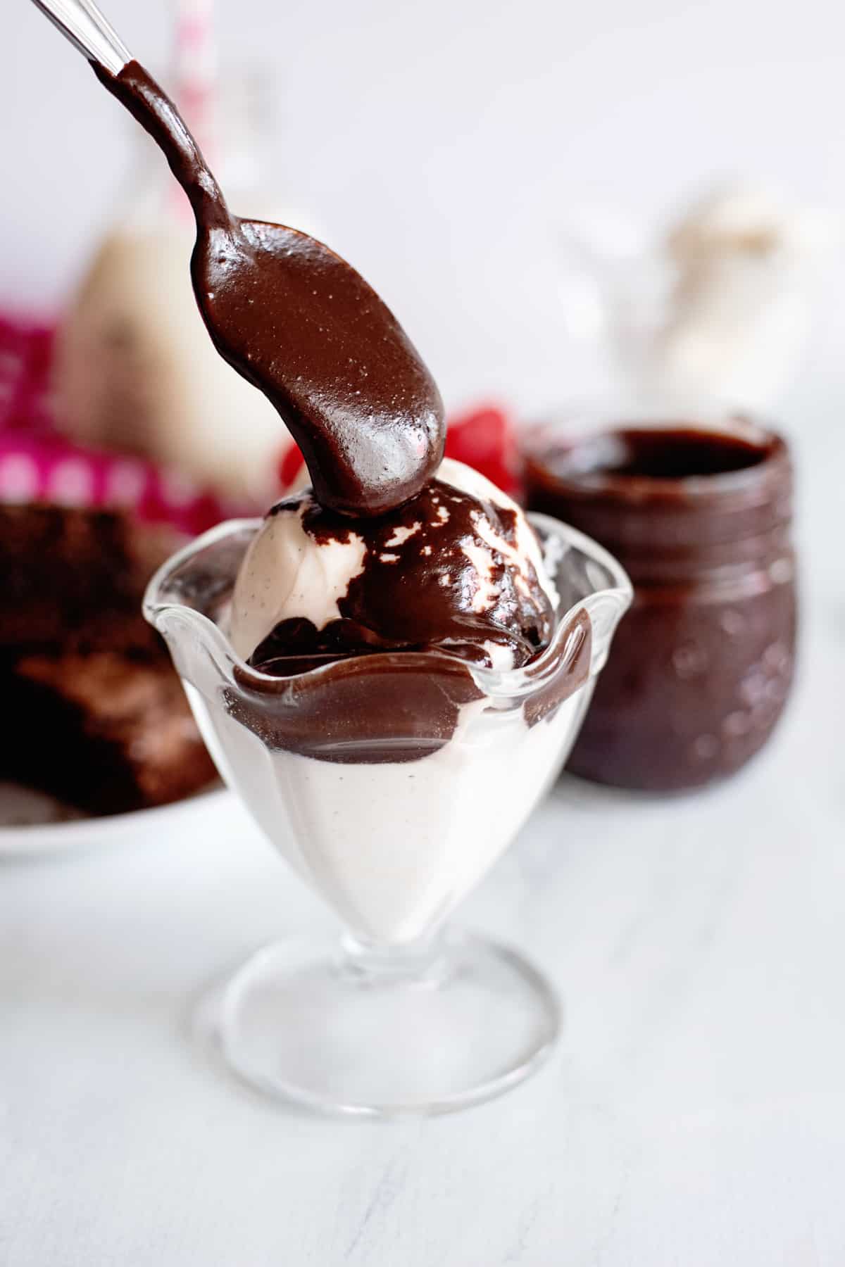 a spoon pouring hot fudge sauce onto ice cream in a sundae dish