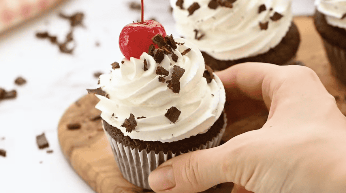 holding a frosted and decorated black forest cupcake.