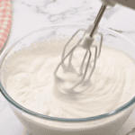 whipping heavy cream to stiff peaks in a glass bowl with a hand mixer.