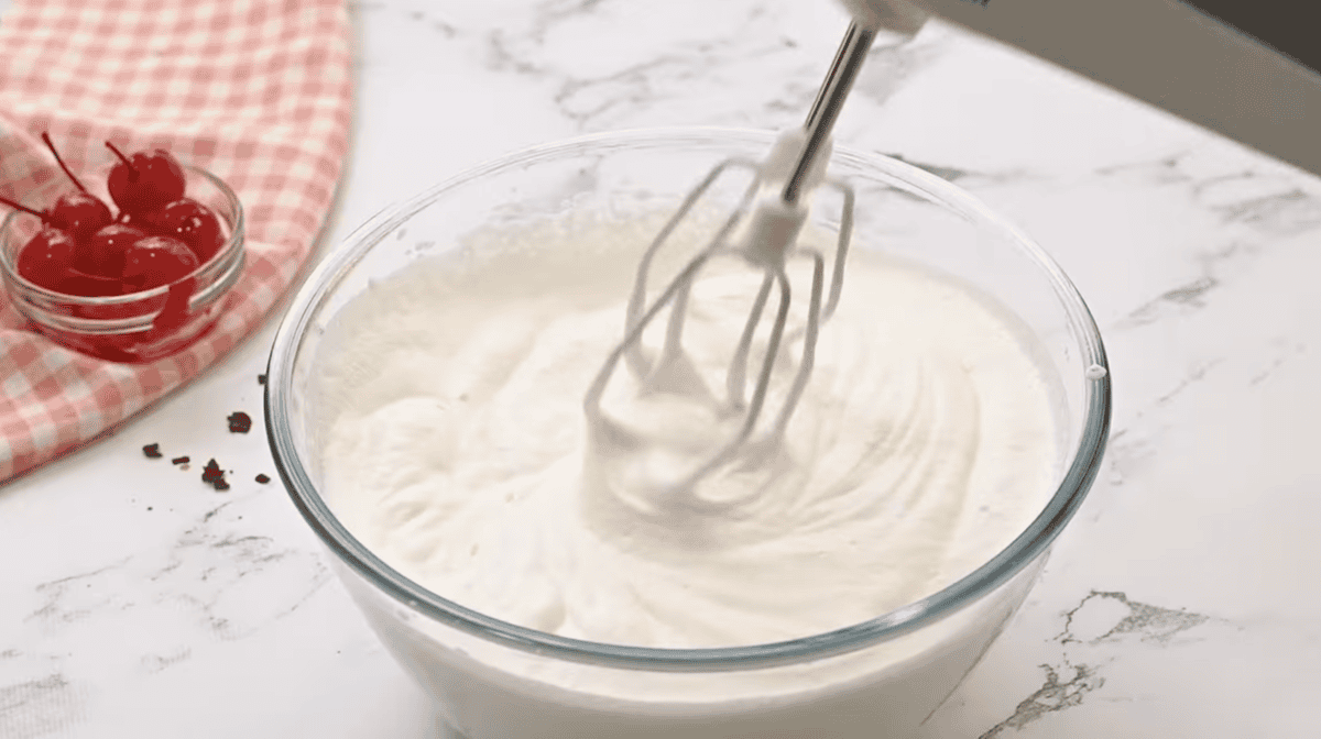whipping heavy cream to stiff peaks in a glass bowl with a hand mixer.
