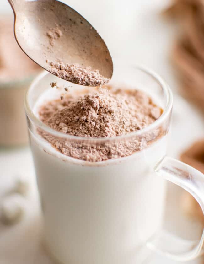 a spoon pouring homemade hot chocolate mix over a glass of milk.