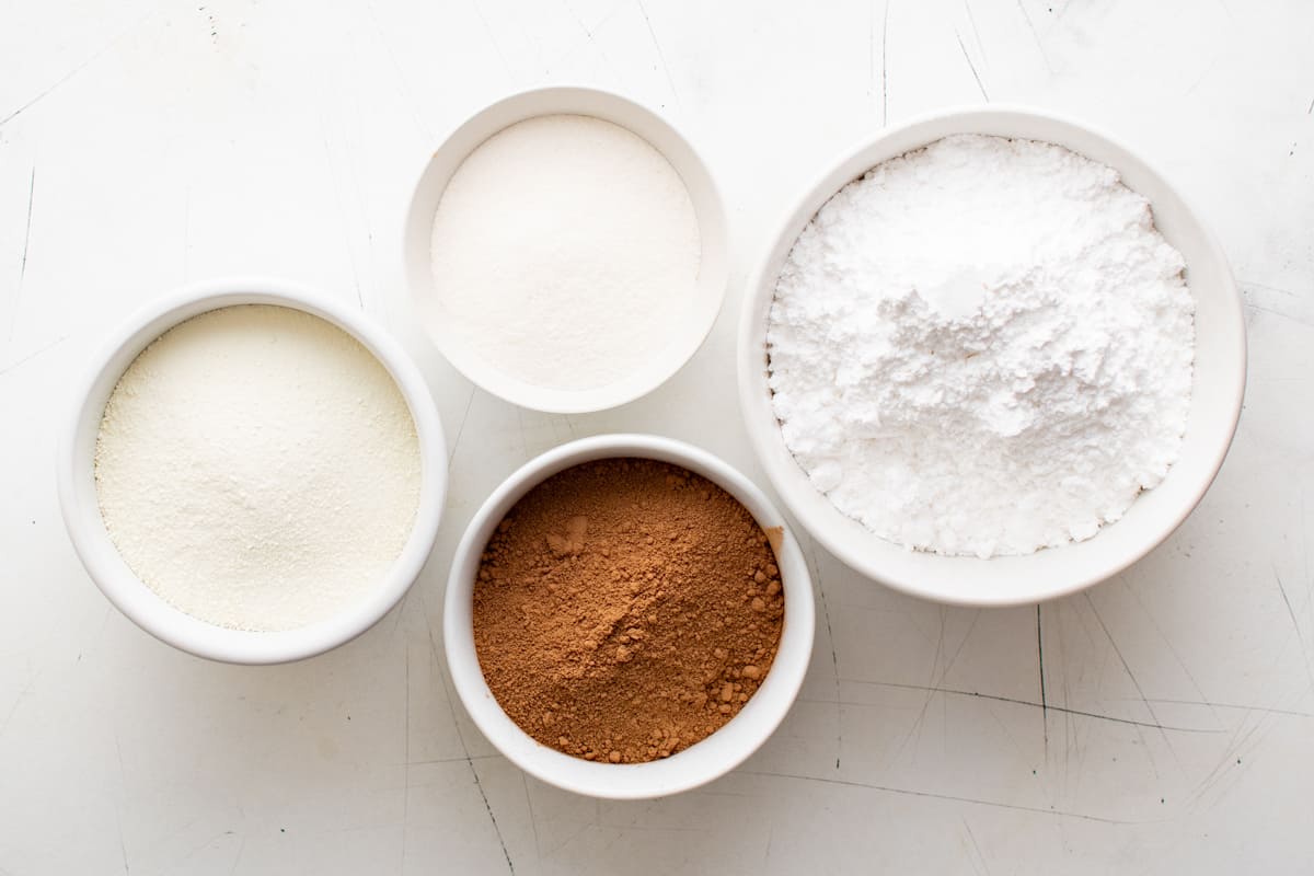 overhead view of ingredients for homemade hot chocolate mix in white bowls.