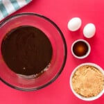 melted butter and chocolate in a glass bowl next to brown sugar, eggs, and vanilla extract.