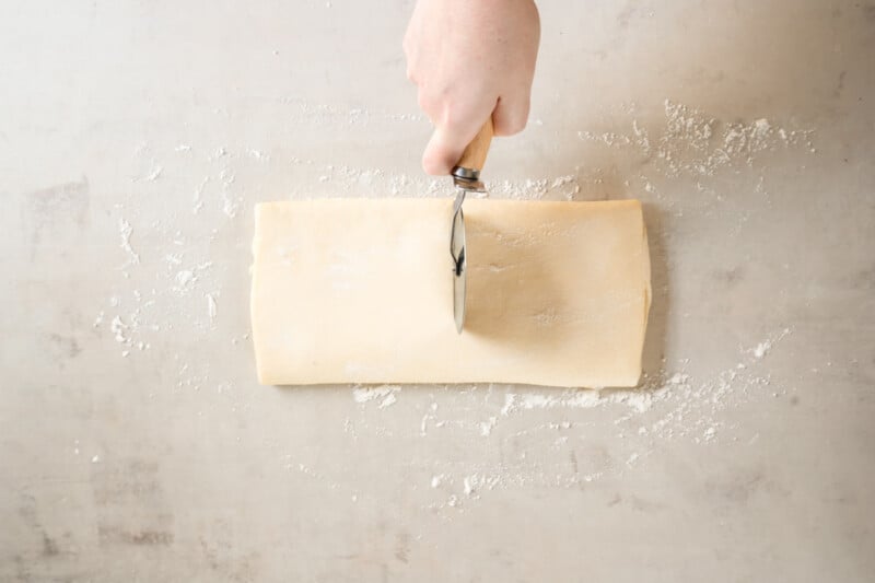a person cutting a piece of dough on a table.